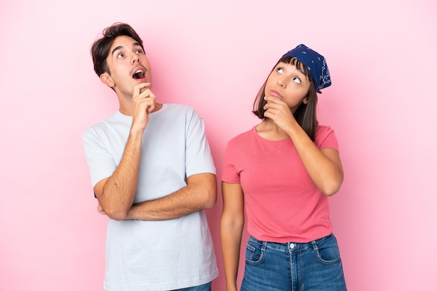 Young couple isolated on pink background thinking an idea while scratching head