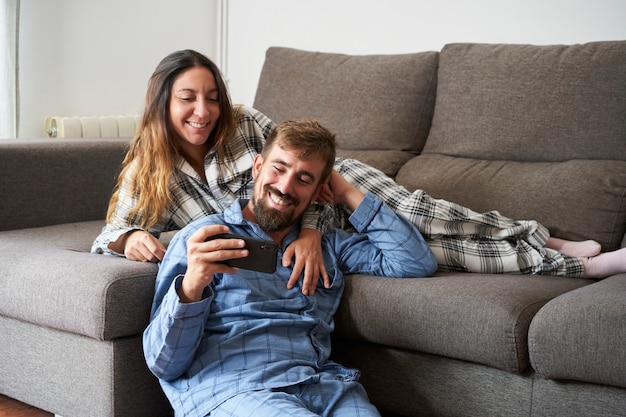 Young couple looking at mobile together, dressed in pajamas at home. They are happy and laughing on a vacation, enjoying being together.