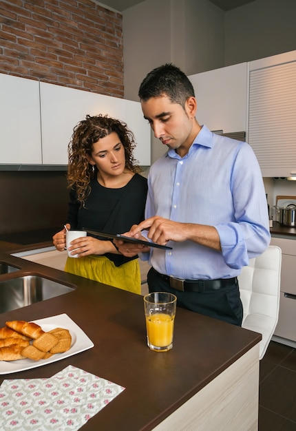 Young couple looking news in electronic tablet while having fast coffee in home before go to work