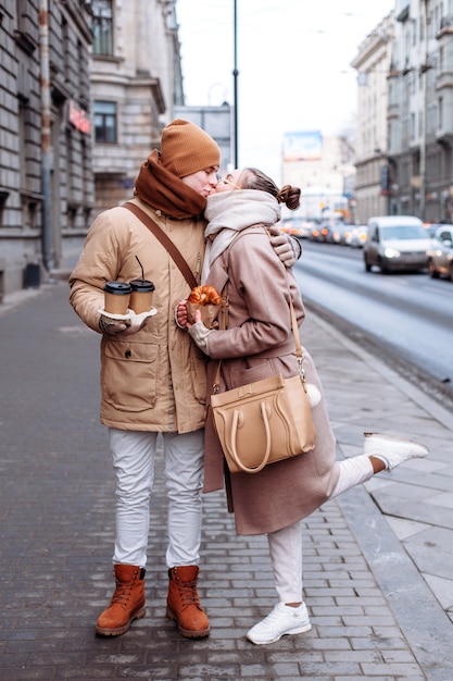 Young couple in love are kissing on the street in cold winter weather. They have coffee and some food.