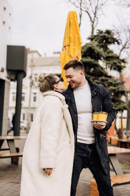 A young couple in love in autumn in outerwear walks on the street and drinks coffee Recreation in the open air Young stylish couple