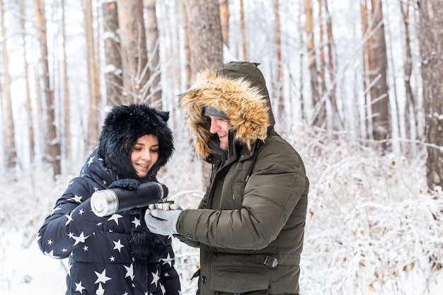 Young couple in love drink a hot drink from a thermos and enjoy winter nature.