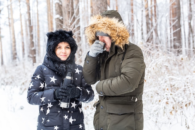 Young couple in love drink a hot drink from a thermos and enjoy winter nature.