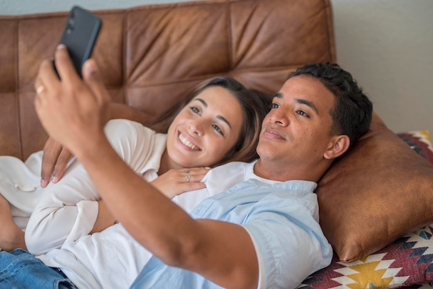 Young couple in love enjoy and use modern mobile phone together laying and relaxing on the sofa Love and relationship young people indoor leisure activity with internet connection Video call concept