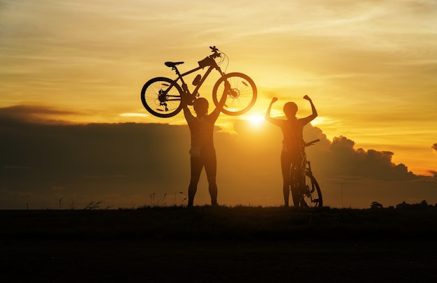 Young Couple in love fun and happy riding mountain bike after covid-19 coronavirus outbreak. End of the coronavirus outbreak. Silhouette cycling man and woman riding mountain bike at sunset time.