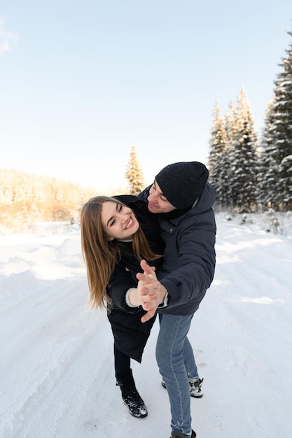 Young couple in love hugging on a snowy road surrounded by forest winter family walks