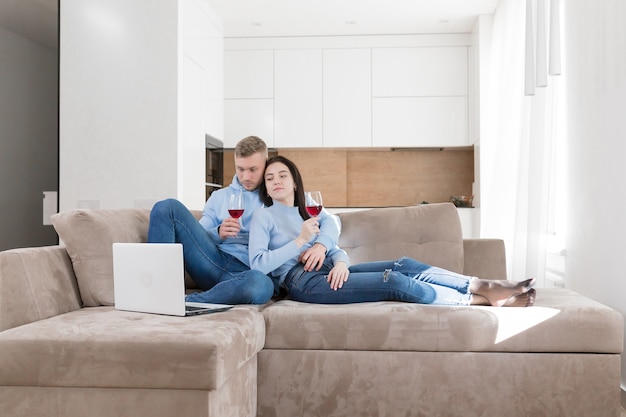 A young couple in love, a man and a woman relaxing on the couch and looking at a laptop