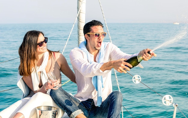 Young couple in love on sailing boat cheering with champagne wine bottle