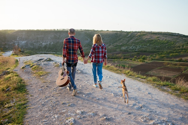 Young couple in love sitting on the park  while these young guitar playing guitar in sunset time. Together with dogs