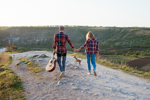 Young couple in love sitting on the park  while these young guitar playing guitar in sunset time. Together with dogs