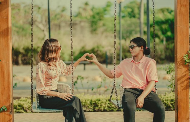 Young couple in love sitting on a swing making a heart shape Happy couple in love on a park swing making a heart shape