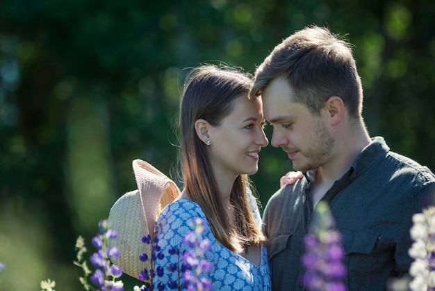 Young couple in love smile and hug in nature in flowers Beautiful park with blooming purple lupins Love and tenderness