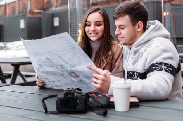 Young couple in love travels, sitting on the table, looking the map of the city, drinking coffee and feeling happy together outdoor