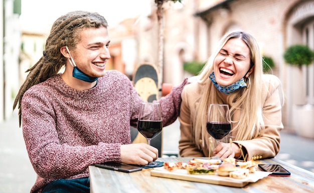 Young couple in love wearing open face mask having fun at wine bar outside