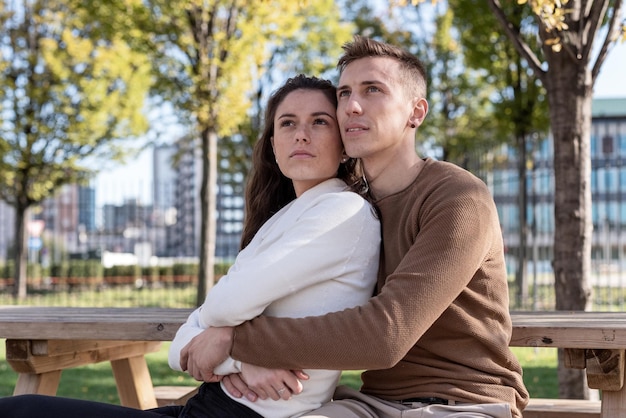 Young couple of lovers hugging on a bench with their eyes on the horizon love concept