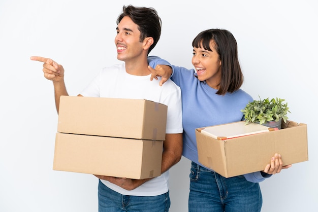 Young couple making a move while picking up a box full of things isolated on white background pointing to the side to present a product