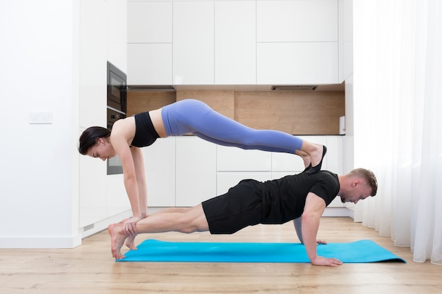 young couple man and woman doing fitness together at home on the floor, two people doing sports exercises in the kitchen on a sports mat