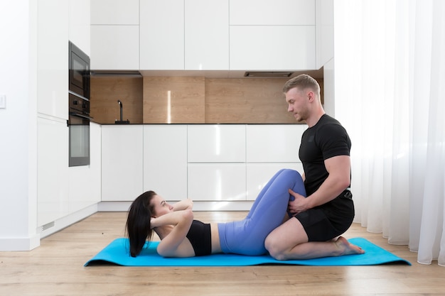 young couple man and woman doing fitness together at home on the floor, two people doing sports exercises in the kitchen on a sports mat