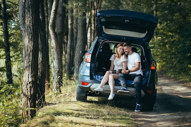 Young couple, man and woman, hugging together on a picnic, sitting in the trunk of a car in the woods, happy together