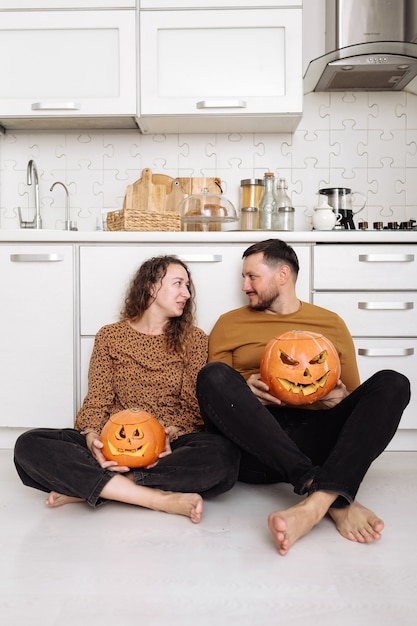 Young couple man and woman sitting on the floor at kitchen at home having fun and preparing for halloween talking laughing cheerful.