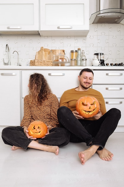 Young couple man and woman sitting on the floor at kitchen at home having fun and preparing for halloween talking laughing cheerful.