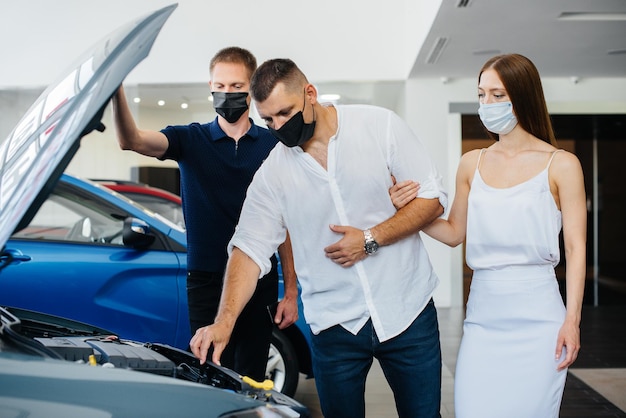 Young couple in masks selects a new vehicle and consult with a representative of the dealership in the period of the pandemic. Car sales, and life during the pandemic.