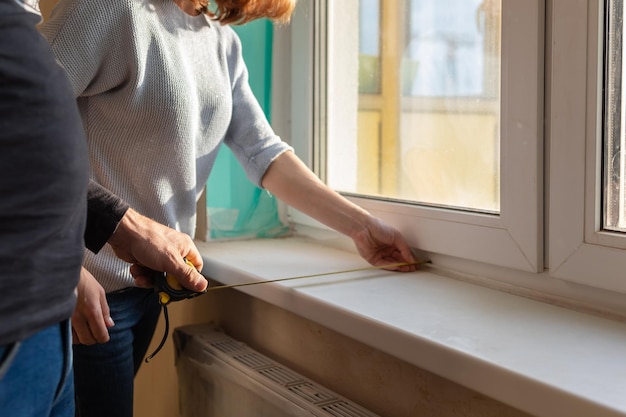 Young couple moving in new apartmen People measure size of window sill with a tape measure Concept new homes new beginning