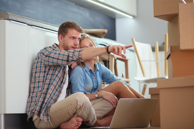 Young couple moving in new home.Sitting and relaxing after unpacking.Looking something on laptop. Young couple.