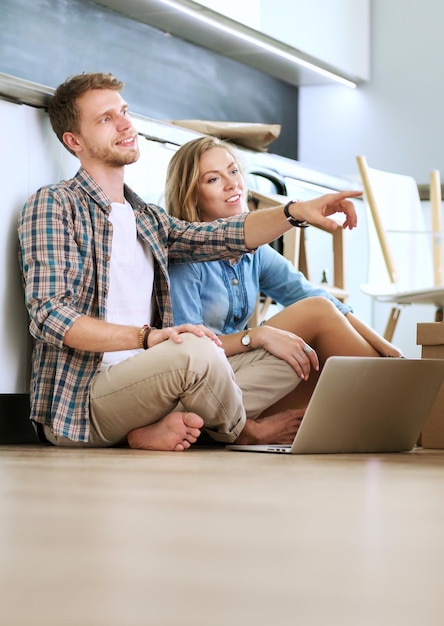 Young couple moving in new homeSitting and relaxing after unpackingLooking something on laptop Young couple