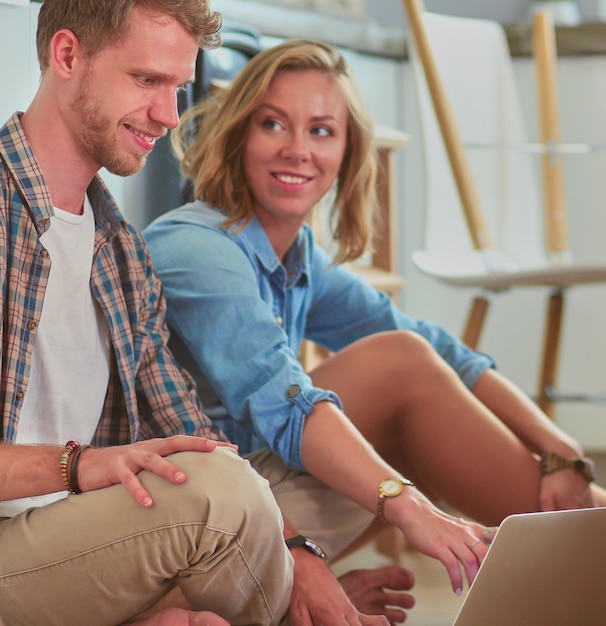 Young couple moving in new homesitting and relaxing after unpackinglooking something on laptop young