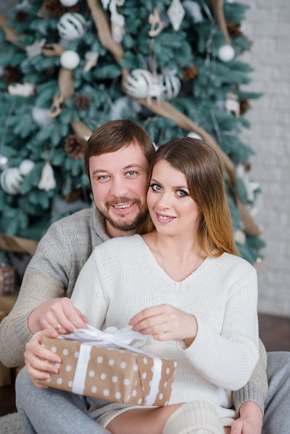 Young couple near Christmas tree. woman with husband. Man hugging girl. New Year present box.