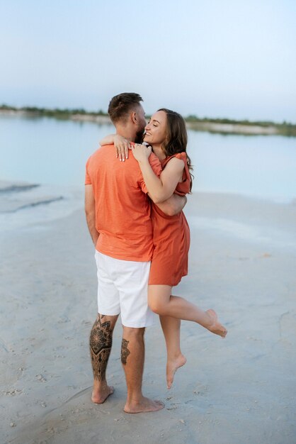 Young couple in orange clothes with dog on an empty sandy beach