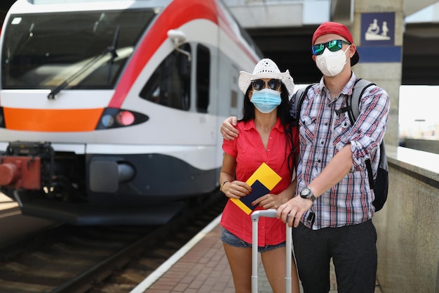 Young couple in protective medical masks standing near train with tickets in their hands