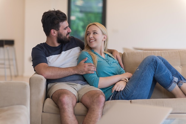 Young couple relaxes on the sofa in the luxury living room, using a laptop and remote control