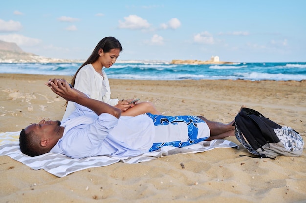 Young couple relaxing on the beach lying sitting on the sand with smartphones