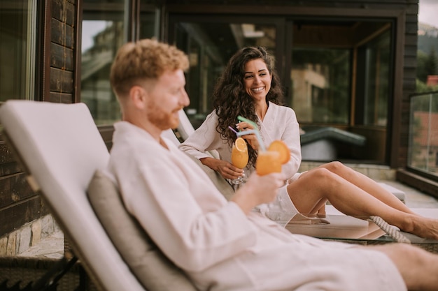 Young couple relaxing on beds and drinking fresh orange juice on the outdoor terrace