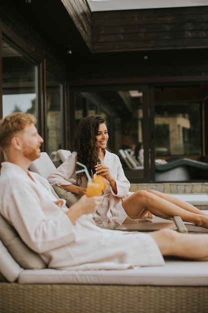 Young couple relaxing on beds and drinking fresh orange juice on the outdoor terrace