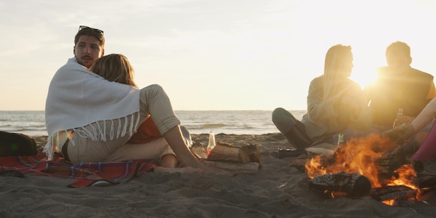 Young Couple Relaxing By The Fire, Drinking A Beer Or A Drink From The Bottle.