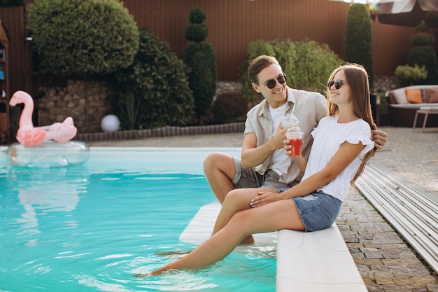 Young couple relaxing in resort swimming pool and drinking cocktails