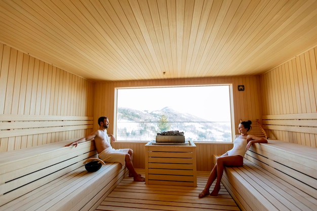 Young couple relaxing in the sauna and watching winter forest through the window