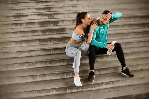 Young couple resting during training with bottle of water in urban environment