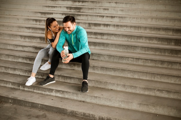 Young couple resting during training with bottle of water in urban environment