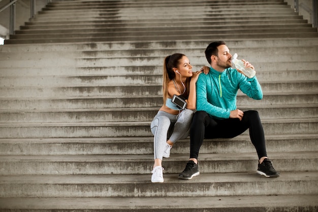 Young couple resting during training with bottle of water in urban environment