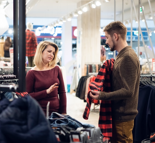 Young couple shopping for clothes in a male department, the girl does not like the shirt her boyfriend has picked