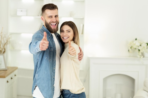 Young Couple Showing Thumbs Up In New House