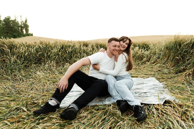 A young couple sits on a bedspread in the middle of a field at sunset. lovers communicate at a romantic meeting. people in the wheat field.