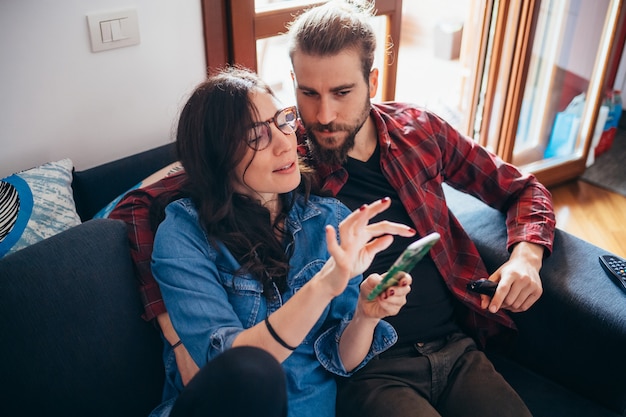 Young couple sitting couch indoor at home looking at smartphone