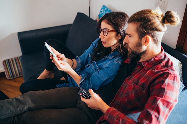 Young couple sitting couch indoor at home using smartphone