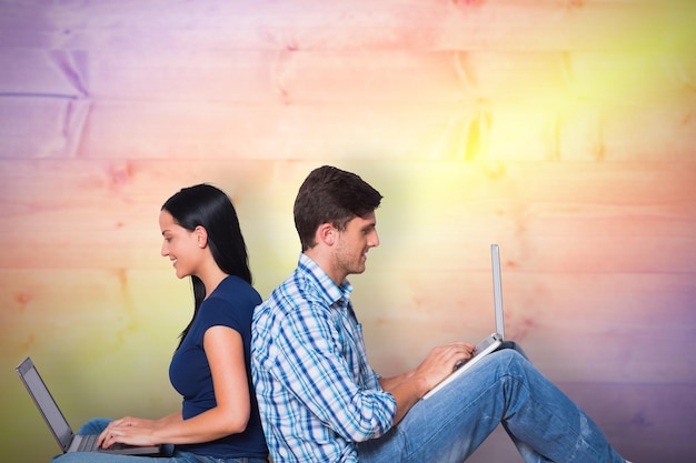 Young couple sitting on floor using laptop against yellow and purple planks