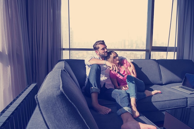 Young couple sitting on sofa near the window watching television together at luxury home